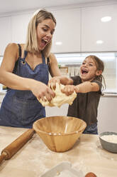 Verspielte Mutter und Tochter schreien beim Kneten von Pizzateig in der Küche zu Hause - VEGF02591