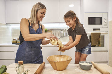 Lächelnde Mutter und Tochter kneten Pizzateig in der Küche zu Hause - VEGF02592