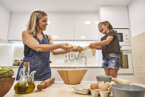 Fröhliche Mutter und Tochter kneten Pizzateig in der Küche zu Hause - VEGF02593