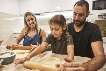 Familie knetet Pizzateig mit Nudelholz auf einem Tisch in der Küche - VEGF02598