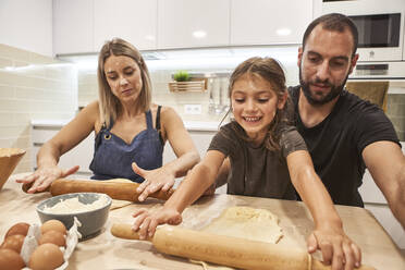 Eltern mit lächelnder Tochter kneten Pizzateig auf einem Tisch in der Küche - VEGF02600