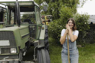 Porträt einer selbstbewussten jungen Frau, die an einem Traktor auf dem Lande steht - GUSF04187