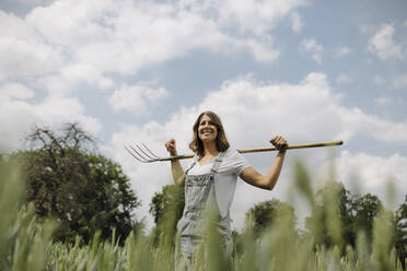 Junge Frau mit Heugabel in einem Getreidefeld auf dem Lande - GUSF04189