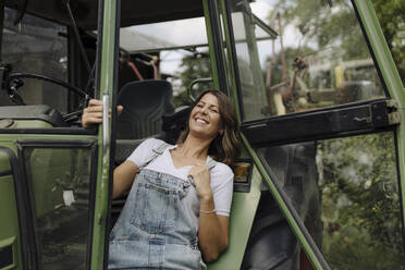 Fröhliche junge Frau an einem Traktor auf dem Lande - GUSF04192