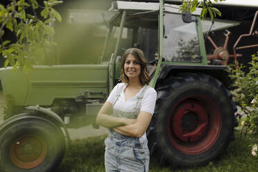 Porträt einer selbstbewussten jungen Frau, die an einem Traktor auf einem Bauernhof steht - GUSF04194