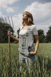 Junge Frau mit Heugabel in einem Getreidefeld auf dem Lande - GUSF04201