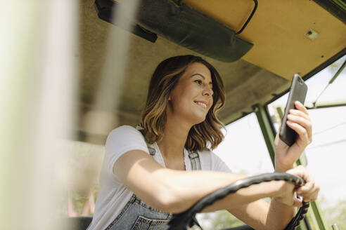 Lächelnde junge Frau, die ein Mobiltelefon in einem Traktor benutzt - GUSF04212