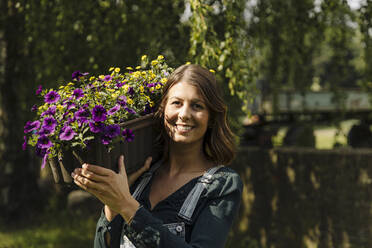 Porträt einer lächelnden jungen Frau mit Blumenkasten - GUSF04218