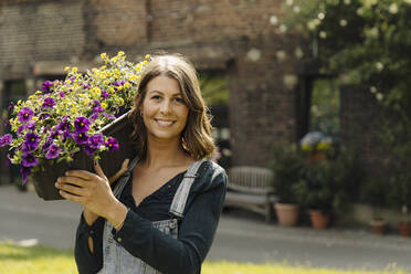 Portrait of smiling young woman carrying flower box - GUSF04219