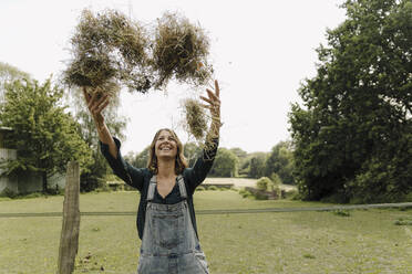 Happy young woman in the countryside throwing up hay - GUSF04228