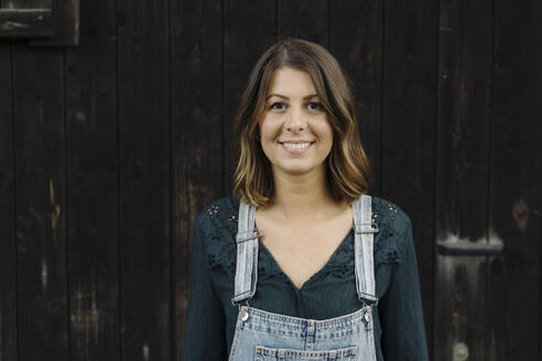 Portrait of a confident young woman in front of a wooden wall - GUSF04230