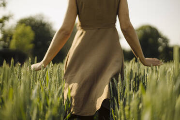Frau in einem Getreidefeld auf dem Lande, die Ähren anfasst - GUSF04255
