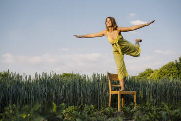 Junge Frau steht auf einem Stuhl in der Natur und tut so, als würde sie fliegen - GUSF04270