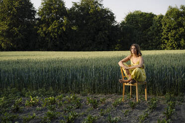 Junge Frau sitzt auf einem Stuhl in der Natur - GUSF04271