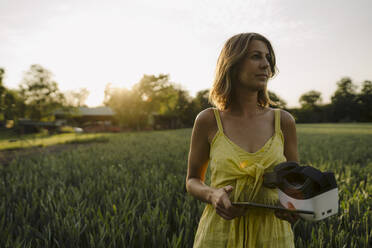 Junge Frau in einem Getreidefeld auf dem Lande mit Tablet und VR-Brille - GUSF04279