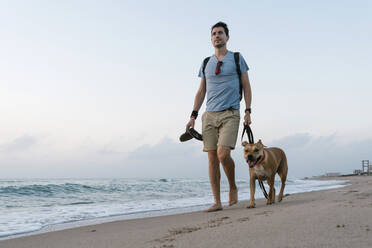 Mann geht mit seinem Hund am Strand spazieren - EGAF00584