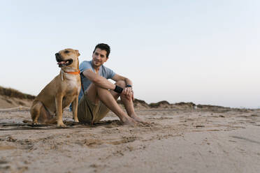 Mann mit seinem Hund am Strand sitzend - EGAF00587
