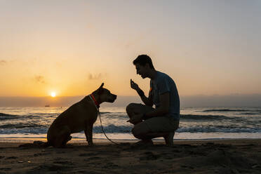 Mann spricht mit seinem Hund am Strand in der Morgendämmerung - EGAF00590