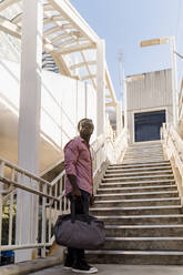 Junger Mann mit Sonnenbrille und Tasche steht auf einer Treppe in Miami, Florida, USA - MAUF03483