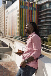 Fröhlicher junger Mann, der sein Smartphone in der Hand hält und wegschaut, während er in der Stadt Miami, Florida, USA, steht - MAUF03490