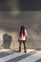 Afro junger Mann mit Dreadlocks steht auf der Straße an der Wand - MAUF03500