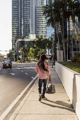 Afro-Mann mit Dreadlocks, der eine Tasche hält, während er auf dem Bürgersteig in Miami, Florida, USA, geht - MAUF03502