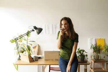 Junge Frau, die am Schreibtisch stehend über ein Smartphone spricht - VABF03201