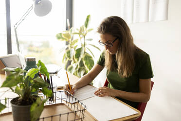 Geschäftsfrau, die im Büro zu Hause sitzt und auf Papier schreibt - VABF03204