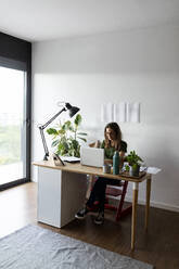 Businesswoman working over laptop on desk in home office - VABF03214