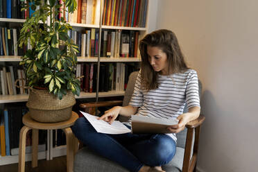 Businesswoman reading document while sitting on chair in home office - VABF03222
