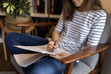 Close-up of businesswoman reading document while sitting on chair in home office - VABF03223