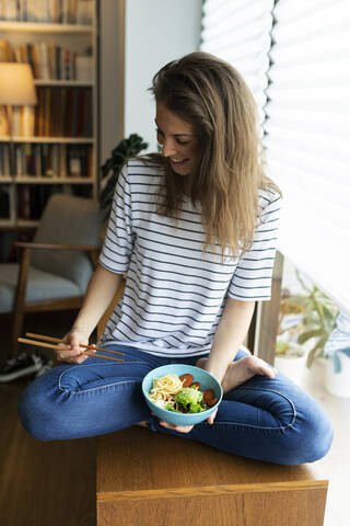 Smiling young woman with food sitting on table at home stock photo