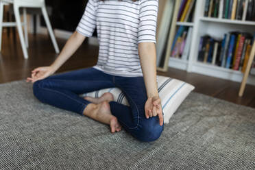 Young woman meditating while sitting on pillow at home - VABF03235