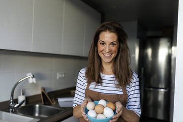 Lächelnde junge Frau hält Eier in der Küche zu Hause - VABF03243