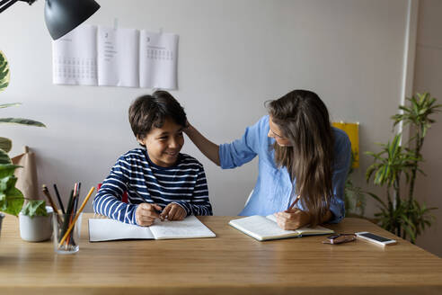 Tutorin im Gespräch mit einem lächelnden Jungen, der am Tisch sitzt - VABF03249