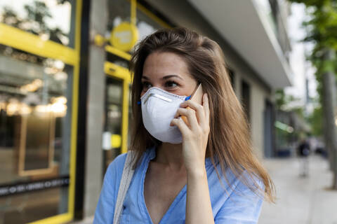 Close-up of young woman wearing mask talking over smart phone in city stock photo