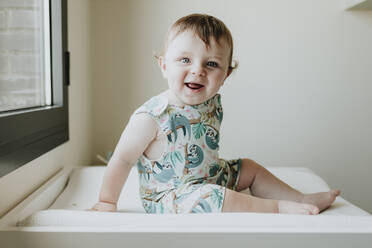 Cute happy baby girl sitting on table at home - GMLF00352