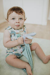Cute baby girl holding toy looking up while sitting at home - GMLF00354