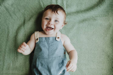 Close-up of cute baby girl laughing while lying on blanket at home - GMLF00356