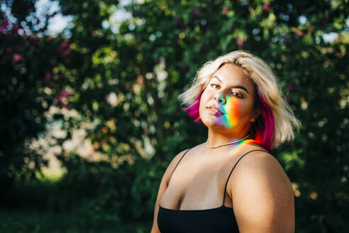 Plus-Size-Frau mit Regenbogenleuchten, die im Park auf ihr Gesicht fällt - DCRF00540