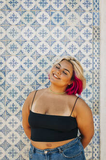 Young woman standing with hand behind back against wall - DCRF00544