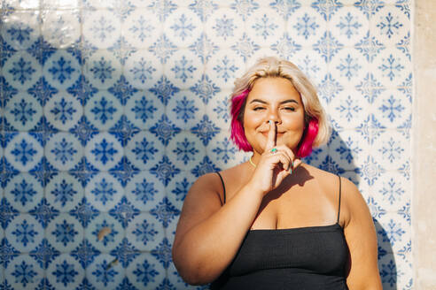 Woman showing silence sign with finger on lips against wall - DCRF00547