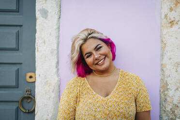 Smiling young woman standing against wall - DCRF00549