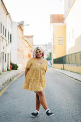 Smiling plus size woman standing with crossed leg on road - DCRF00555