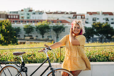 Glückliche Plus-Size-Frau mit Fahrrad lehnt an Parkzaun - DCRF00557