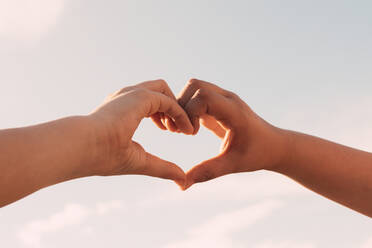 Two sisters joining hands in the shape of a heart in the background of the blue sky, Family - CAVF87489