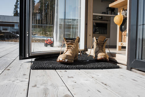 Männerstiefel auf einer Matte an der Hintertür auf einem Balkon zu Hause - CAVF87587