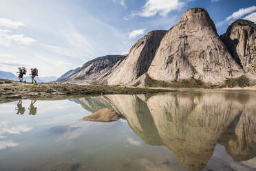 Reflection of two backpackers hiking below steep mountains - CAVF87630