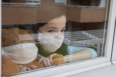 Girl with face mask looking out the window quarantined by coronavirus - CAVF87638