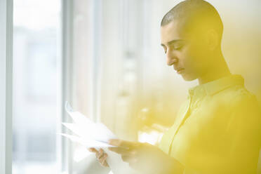 Businesswoman reading papers at the window in loft office - KNSF08196